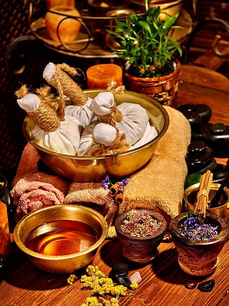 Spa and wellness setup with garlic, herbs in golden bowl, essential oils, dried flowers, and natural ingredients on wooden surface
