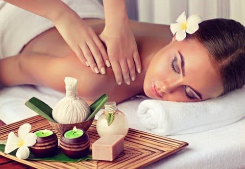Woman receiving a back massage at a spa with candles, flowers, and aromatherapy oils