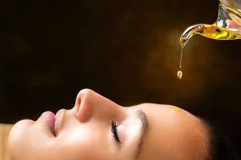Woman receiving facial oil treatment with drop falling onto her face against dark background