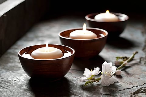 Three wooden bowls with floating white candles arranged in a row on a dark surface with white flowers